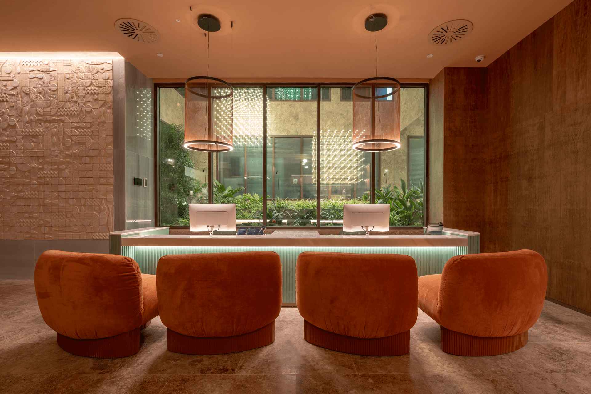 Recepción del ME by Meliá Málaga con sistemas de cerramiento STRUGAL Mostrador de recepción del ME by Meliá Málaga con grandes ventanales de aluminio STRUGAL, sillones naranjas y vista al patio interior