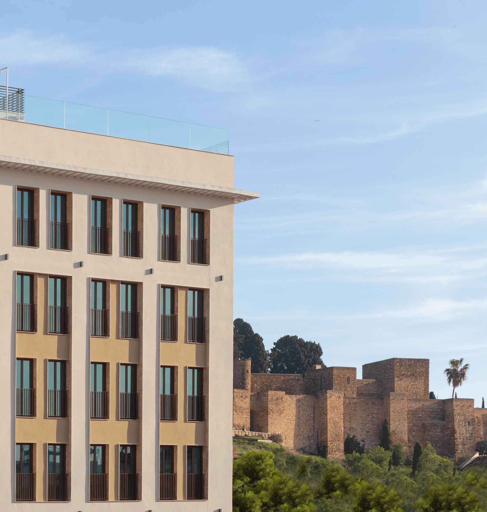 ME by Meliá Málaga junto a la Alcazaba Lateral del edificio ME by Meliá Málaga con la Alcazaba de Málaga al fondo bajo un cielo azul